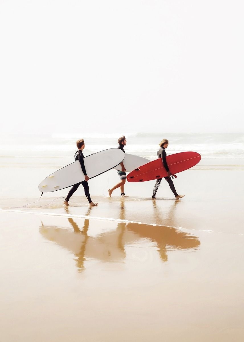 Tres surfistas caminando por la orilla con sus tablas, una de ellas roja