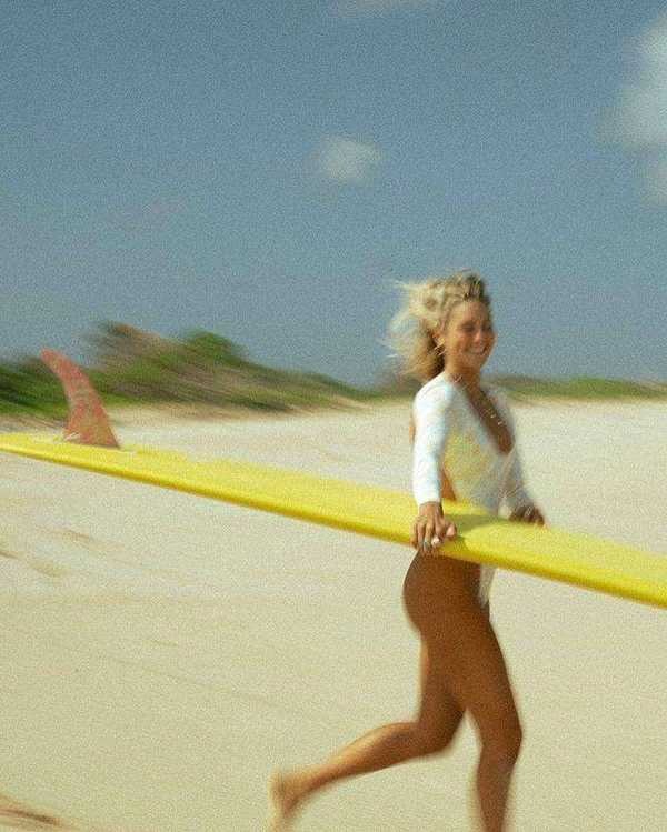 Voluntaria caminando descalza por la duna de La Barrosa con su tabla de surf amarilla